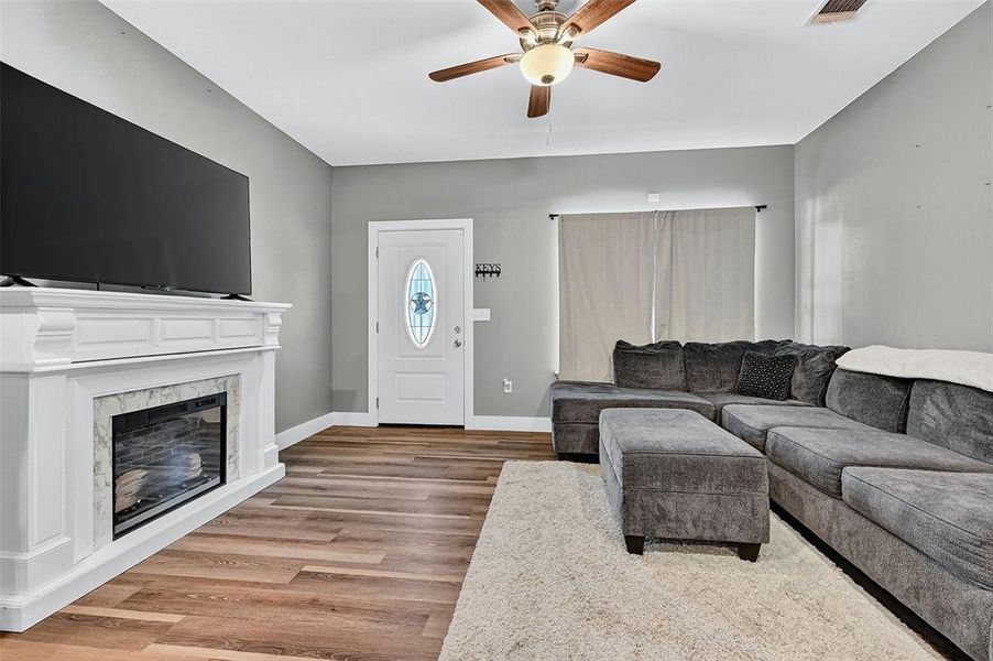 Living room featuring a ceiling fan, wood finished floors, and a high end fireplace Living room featuring a ceiling fan, wood finished floors, and a high end fireplace