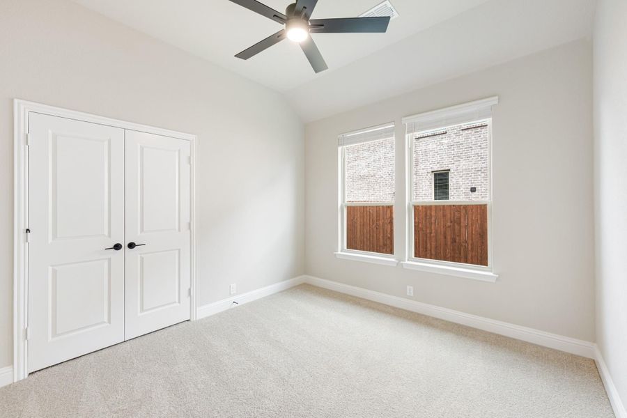 Empty bedroom with carpet, ceiling fan, double closet doors, and two windows