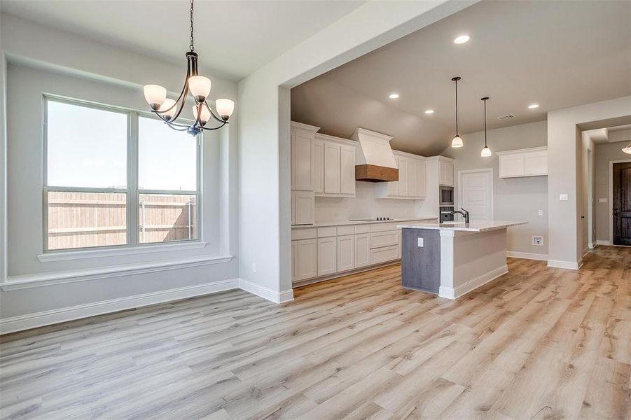 Kitchen featuring white cabinetry, light hardwood / wood-style flooring, premium range hood, a kitchen island with sink, and decorative light fixtures