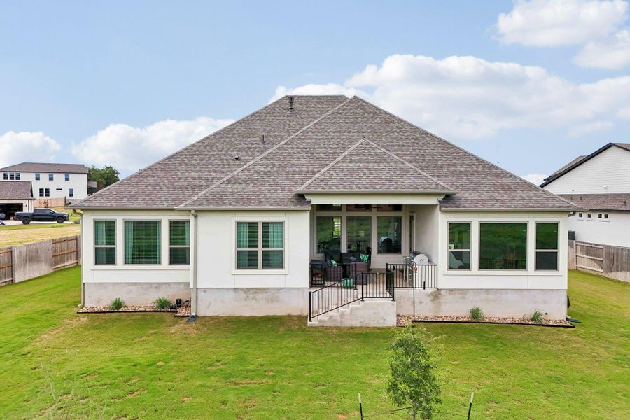 Rear exterior featuring a covered patio, multiple large windows, and a sloped backyard with a wooden fence boundary Rear exterior featuring a covered patio, multiple large windows, and a sloped backyard with a wooden fence boundary