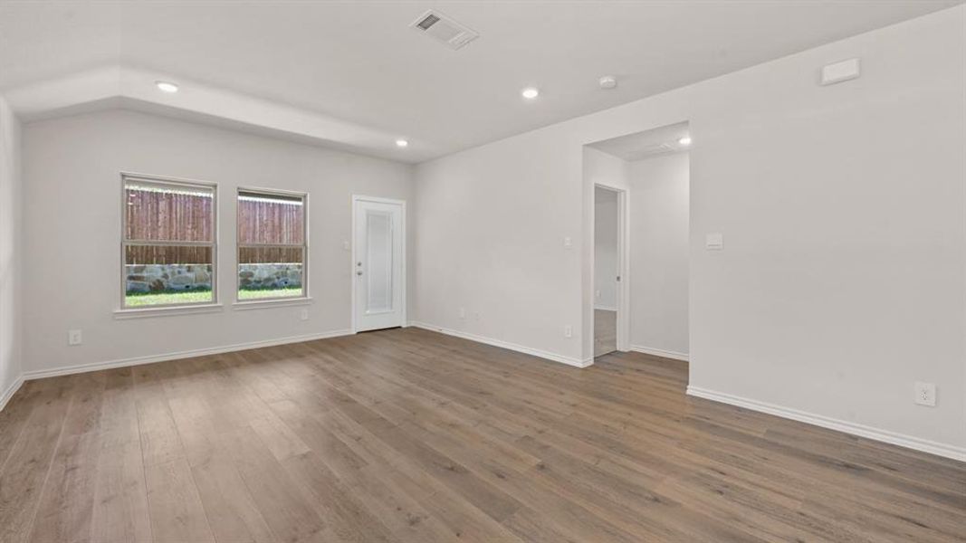 Spacious room featuring wood-finish flooring, recessed lighting, and a vaulted ceiling
