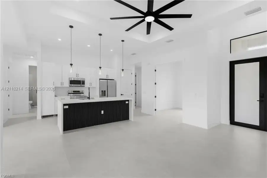 Kitchen featuring a center island with slat detailing and a solid-surface countertop, white cabinetry, integrated stainless steel appliances, large-format tile flooring, and a coffered ceiling with a multi-blade ceiling fan