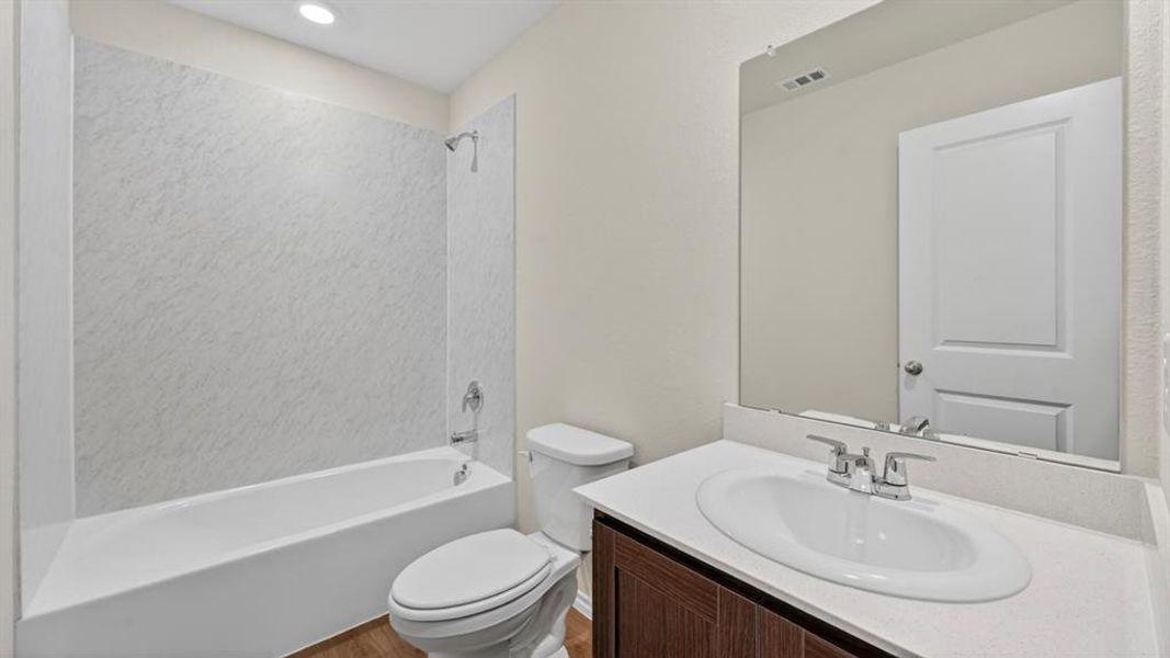 Bathroom featuring a white bathtub with a textured surround, a toilet, and a vanity with a white countertop and dark wood-finish cabinetry