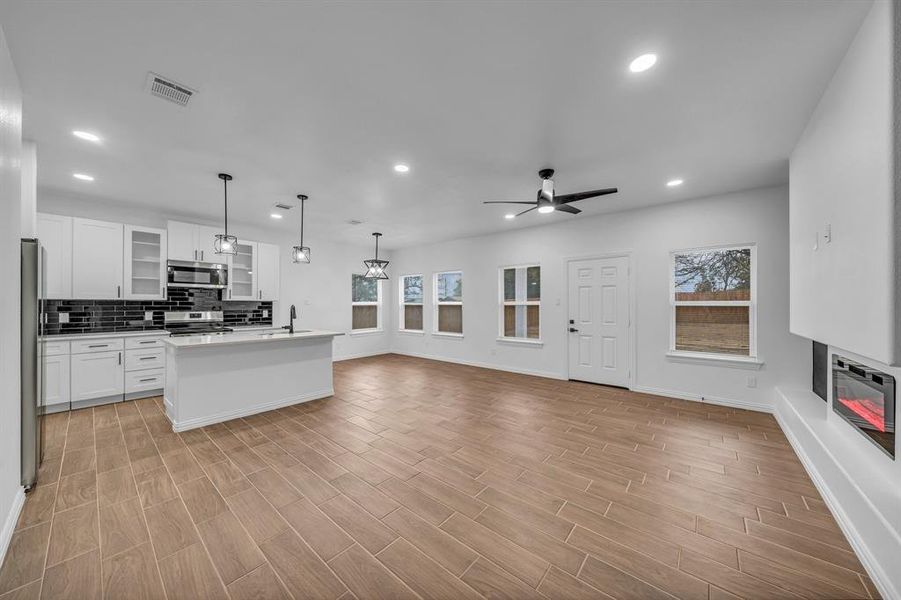 Kitchen with white cabinetry, appliances with stainless steel finishes, an island with sink, pendant lighting, and backsplash