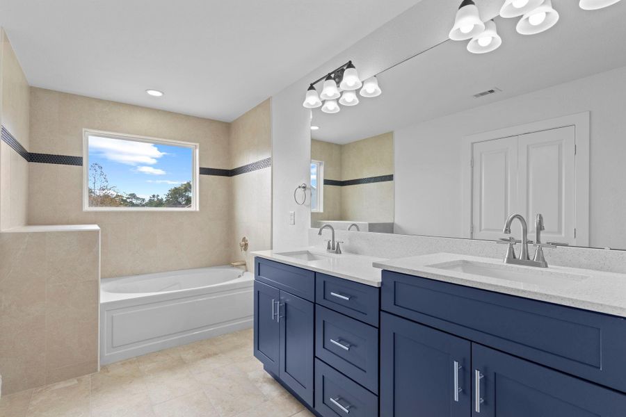 Primary spa retreat has custom cabinetry with cabinets and drawers for all your storage, do not see that much in most primary suites but you do with the Custom home by Next Vista Homes!  Notice the deep soaker tub with ceiling to floor the beautiful tile surroundings with a splash of custom insert for that timeless style!