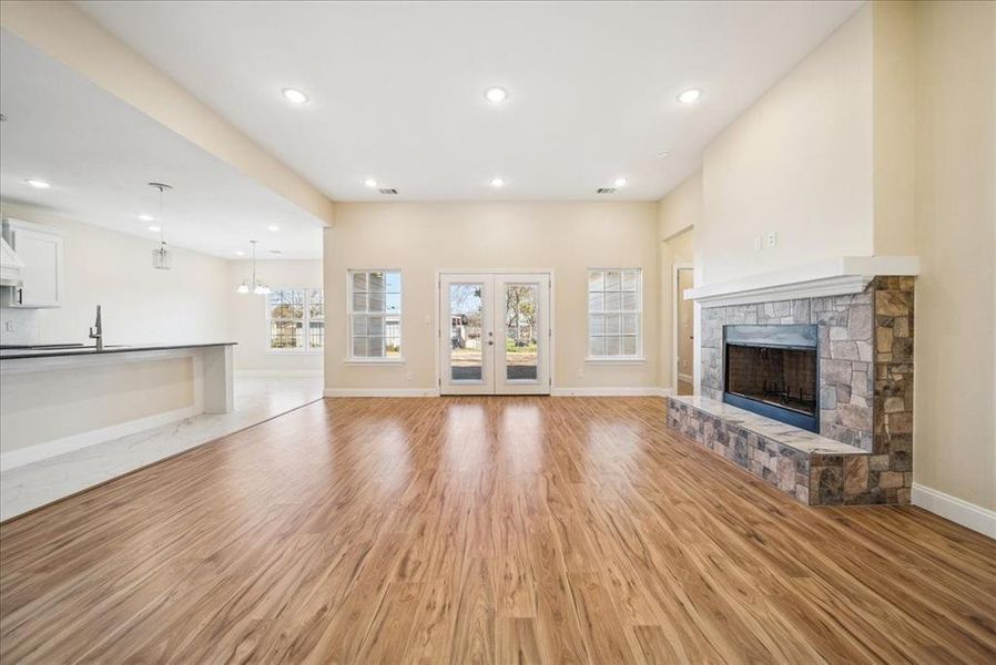 Unfurnished living room with french doors, sink, light hardwood / wood-style flooring, a notable chandelier, and a stone fireplace