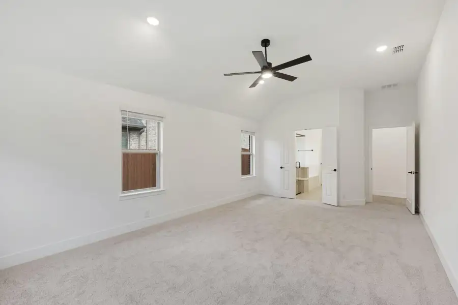 Spacious bedroom with vaulted ceiling, ceiling fan, carpet flooring, and open doors to ensuite bathroom and closet.