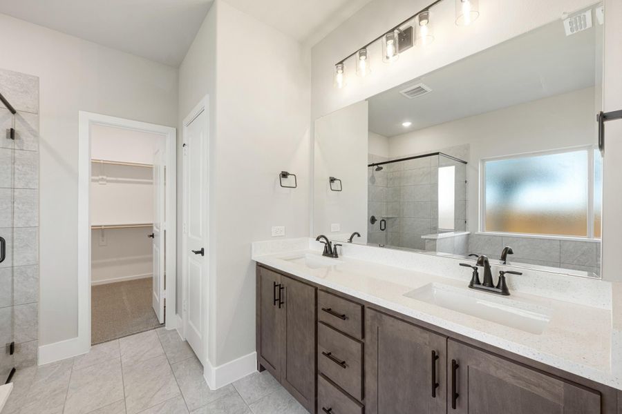 Bathroom with double sink vanity, dark wood cabinets, glass shower, and walk-in closet entrance