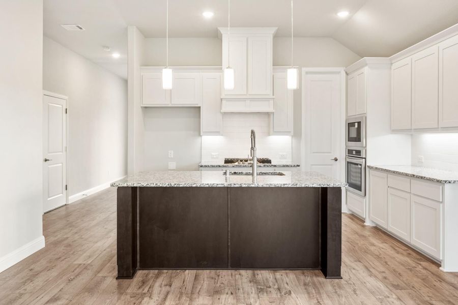 Kitchen with white cabinets, dark island with granite countertop, pendant lights, and light wood floors Kitchen with white cabinets, dark island with granite countertop, pendant lights, and light wood floors