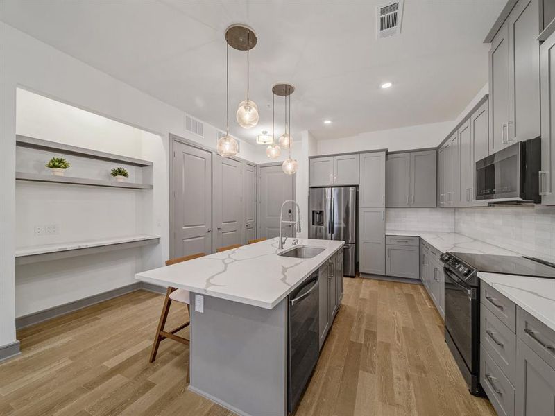 Kitchen with stainless steel appliances, recessed lighting, a kitchen island with sink, hanging light fixtures, and gray cabinets
