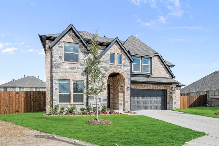 Two-story home with brick and stone exterior, arched entry, two-car garage, and green front lawn