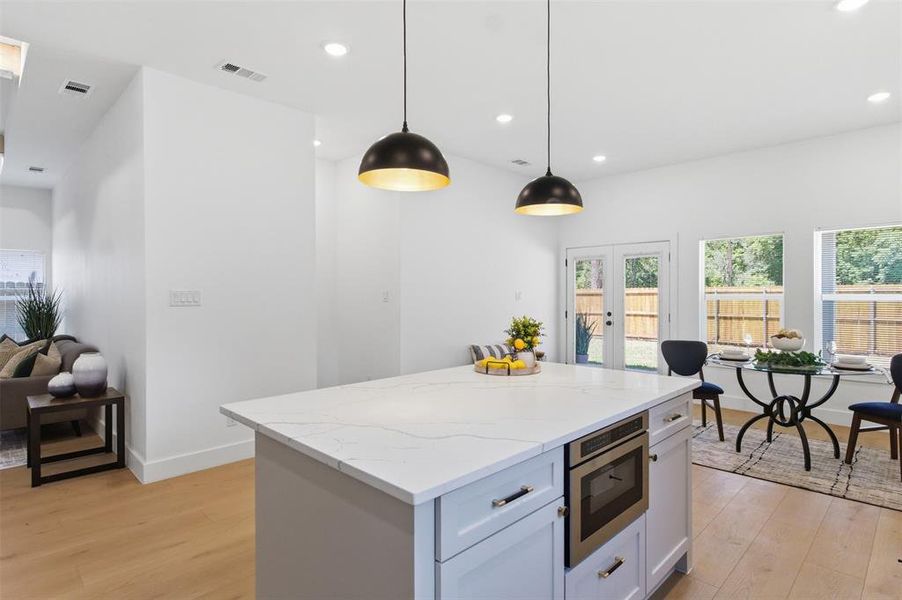 Modern kitchen island featuring a light-toned countertop, under-counter microwave, and pendant lighting