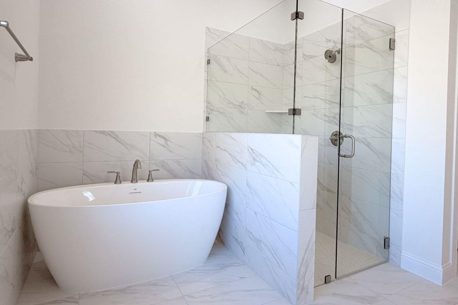 Bathroom featuring a marble finish shower, light marble finish floors, a freestanding tub, and tile walls