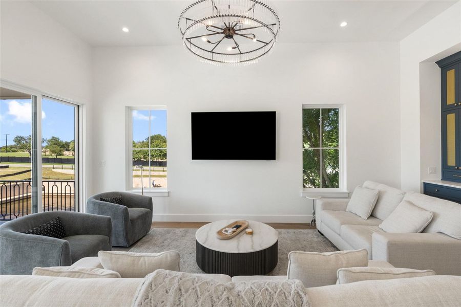 A refined living area boasts an elegant chandelier and rich hardwood flooring, with abundant natural light from large windows and glass doors. A refined living area boasts an elegant chandelier and rich hardwood flooring, with abundant natural light from large windows and glass doors.
