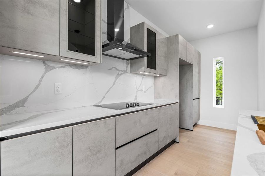 Kitchen with wall chimney range hood, glass insert cabinets, modern cabinets, light wood-type flooring, and black electric cooktop
