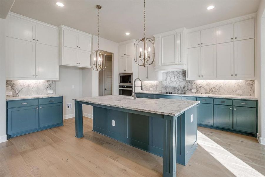 Kitchen with decorative backsplash, a center island with sink, white cabinets, and light hardwood / wood-style floors