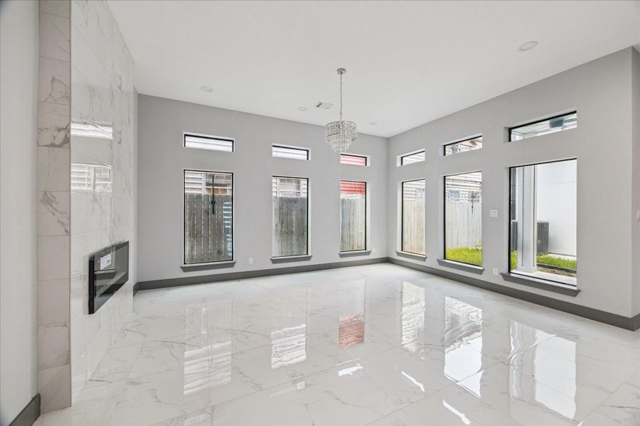The living room offers an open, airy feel, with tall windows, sleek tile flooring, a standout chandelier, and a modern fireplace feature. The living room offers an open, airy feel, with tall windows, sleek tile flooring, a standout chandelier, and a modern fireplace feature.