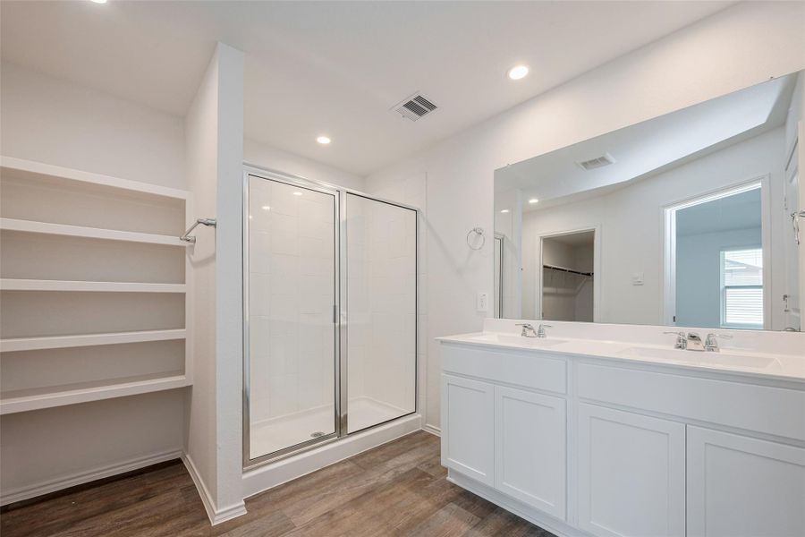 The ensuite bathroom boasts a dual-sink vanity with white cabinetry and a wide mirror above. A separate glass-enclosed shower sits beside open shelving. The ensuite bathroom boasts a dual-sink vanity with white cabinetry and a wide mirror above. A separate glass-enclosed shower sits beside open shelving.