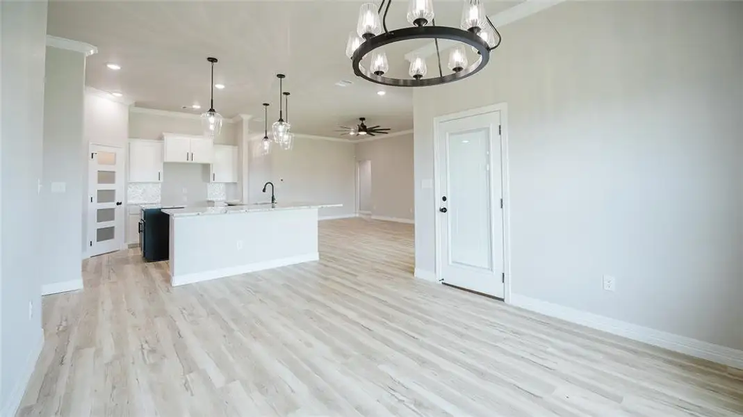 Kitchen featuring open floor plan, light wood-style flooring, ornamental molding, backsplash, and a center island with sink Kitchen featuring open floor plan, light wood-style flooring, ornamental molding, backsplash, and a center island with sink