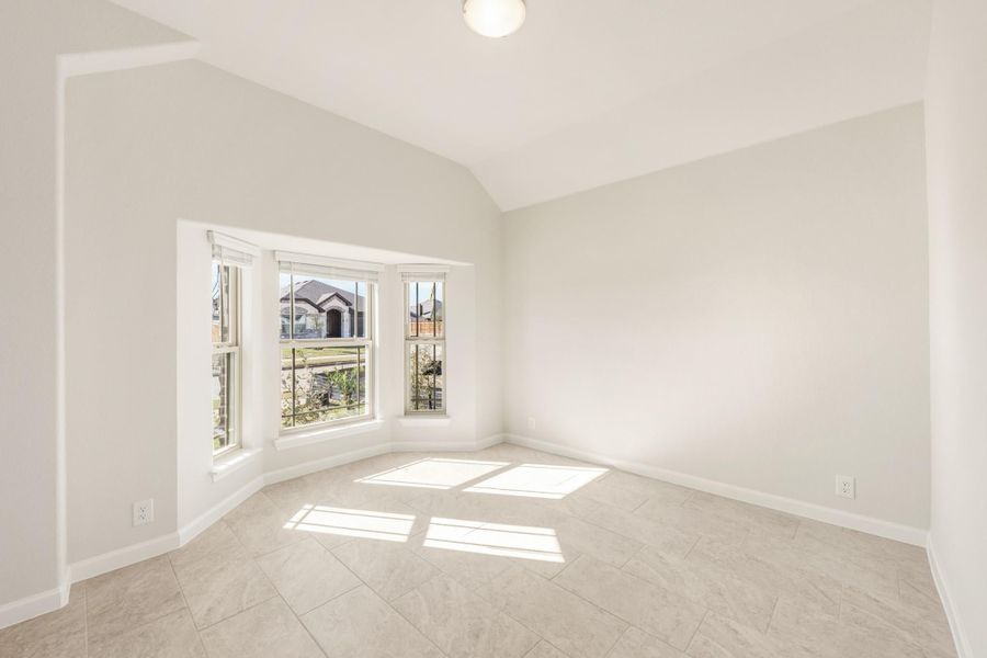 Empty room with vaulted ceiling, bay window, and light tile floors