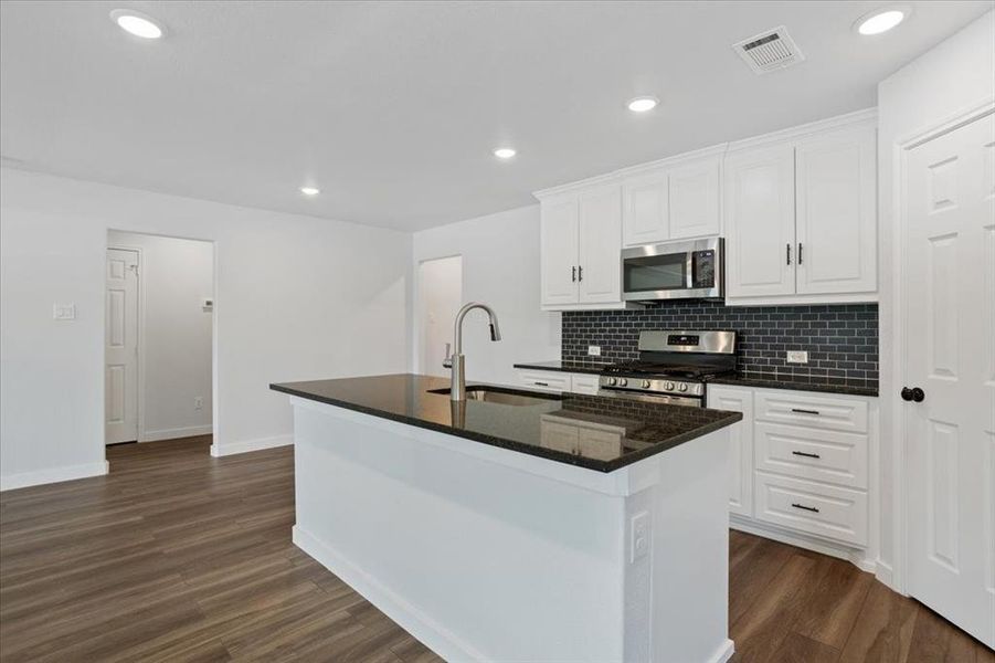 Kitchen featuring stainless steel appliances, white cabinets, sink, an island with sink, and dark hardwood / wood-style flooring