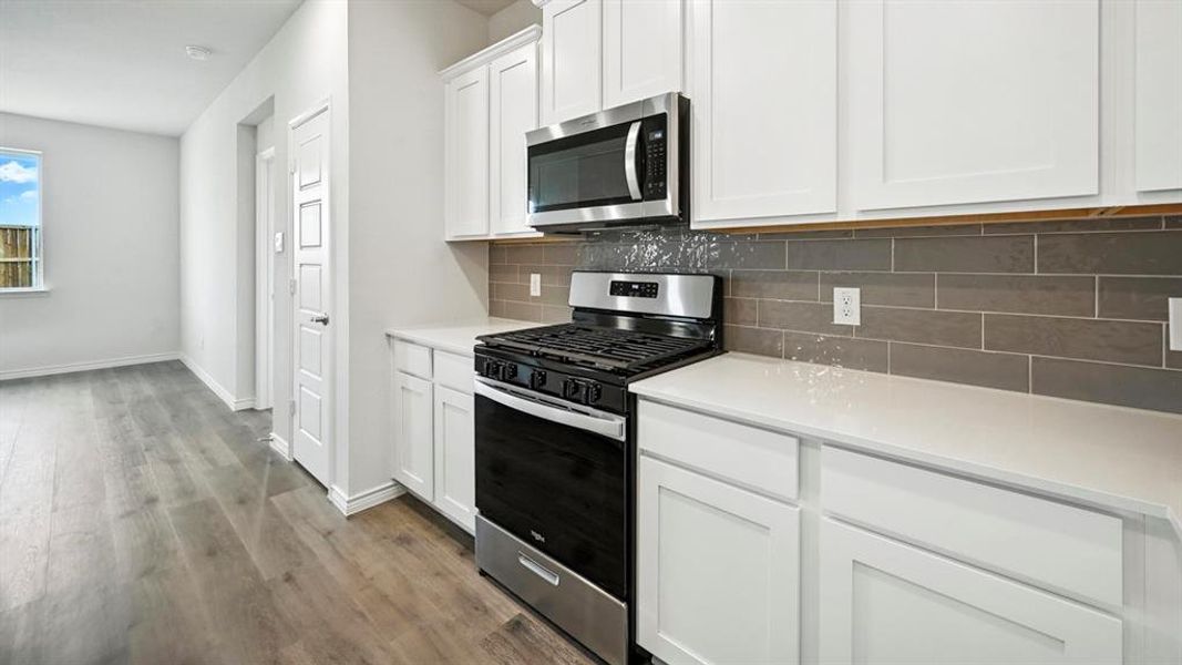 Modern kitchen featuring white shaker cabinetry, stainless steel appliances, light countertops, and a gray subway tile backsplash