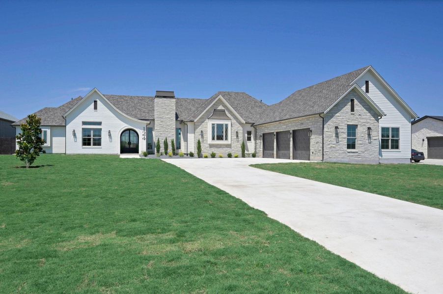 French country home with a front lawn, brick siding, concrete driveway, and roof with shingles
