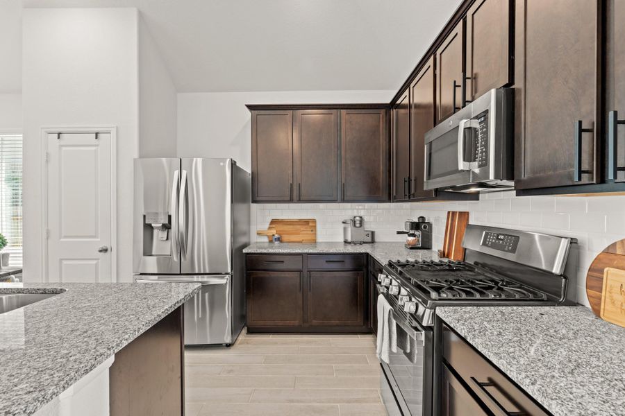You'll love the details of this kitchen! It features black cabinet hardware, sleek white tile backsplash, granite countertops, and a pantry!
