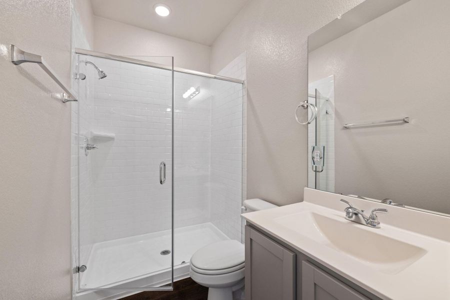 Full bathroom with a textured wall, vanity, a shower stall, and dark wood-type flooring