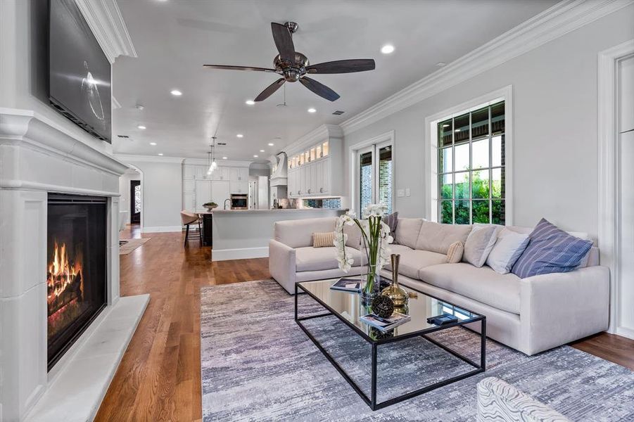 Living area with crown molding, wood finished floors, a warm lit fireplace, recessed lighting, and a ceiling fan Living area with crown molding, wood finished floors, a warm lit fireplace, recessed lighting, and a ceiling fan
