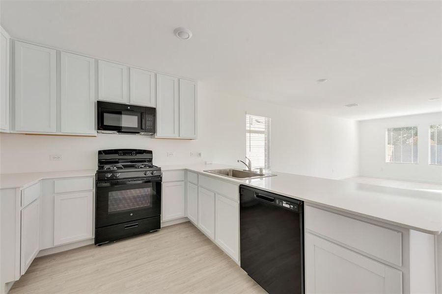 Kitchen with white cabinets, sink, black appliances, and kitchen peninsula