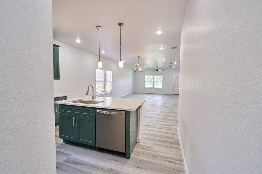 Kitchen island featuring a stainless steel sink with a high-arc faucet, integrated dishwasher, and pendant lighting