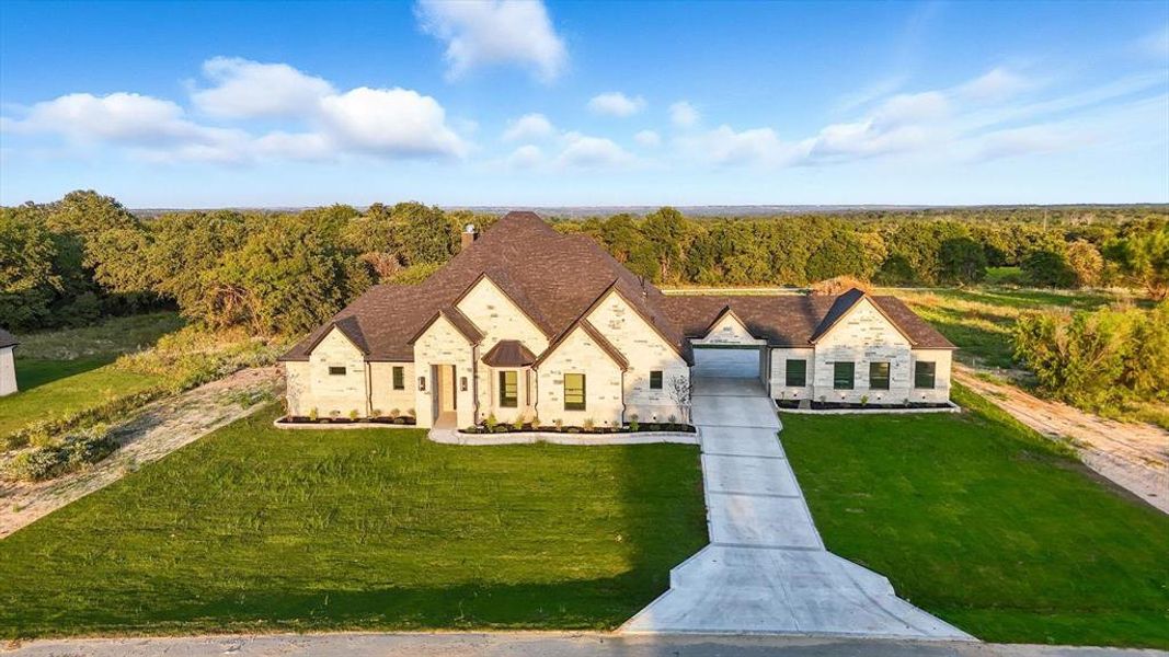 French country home with a front yard, stone siding, a wooded view, and a chimney French country home with a front yard, stone siding, a wooded view, and a chimney