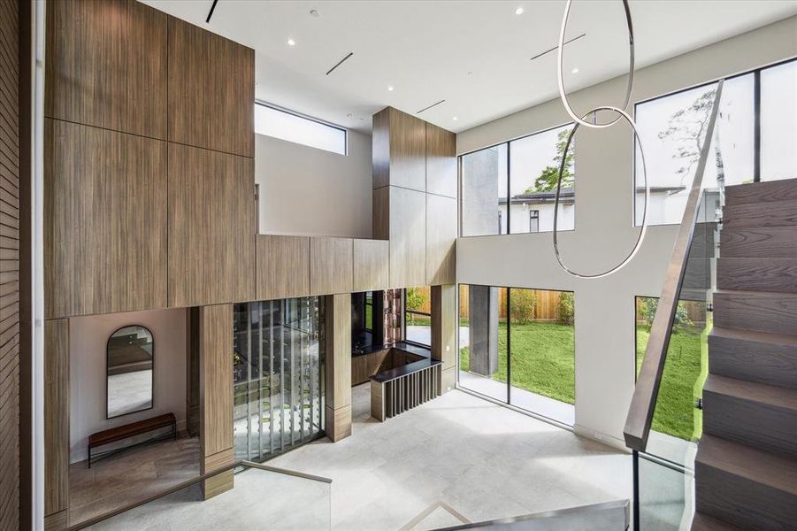 The double-height foyer is a breathtaking sight, adorned with custom paneled walls and a wall of windows that flood the space with natural light and offer expansive views of the backyard. A designer chandelier hangs elegantly, acting as a striking piece of art that complements the grandeur of this exquisite entryway.