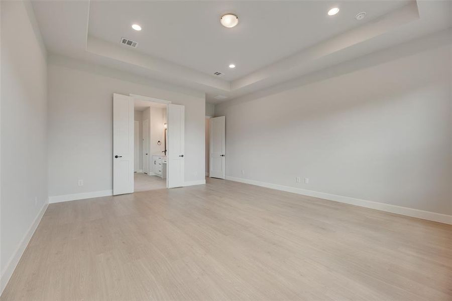 Unfurnished room with a raised ceiling, light wood-style flooring, and recessed lighting