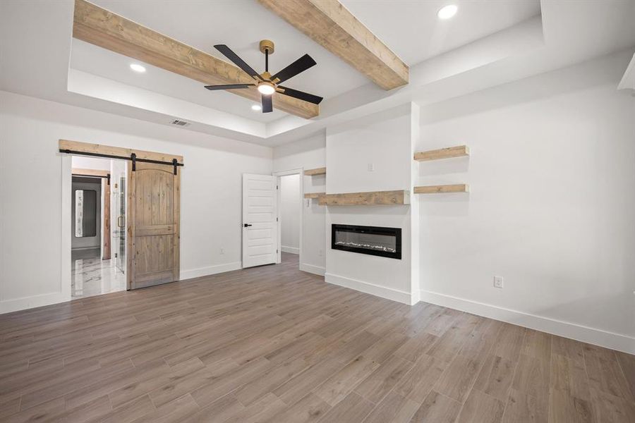 Spacious interior with wood-finish flooring and a tray ceiling featuring exposed wood beams and recessed lighting