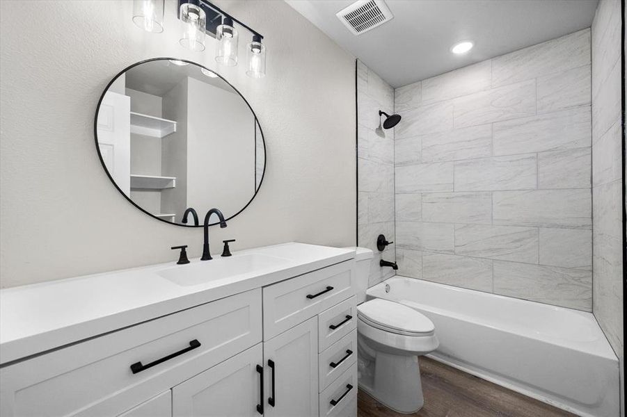 Bathroom featuring a white vanity with matte black hardware, a circular mirror, and a white bathtub with light-toned tiled walls