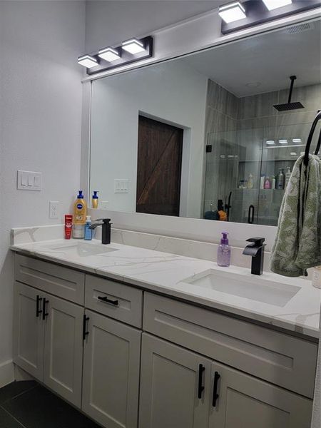 Bathroom with double vanity, a stall shower, and dark tile patterned flooring