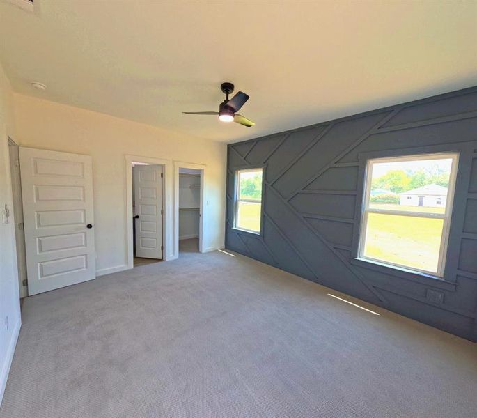 Unfurnished bedroom with a spacious closet, carpet floors, a decorative wall, and ceiling fan Unfurnished bedroom with a spacious closet, carpet floors, a decorative wall, and ceiling fan