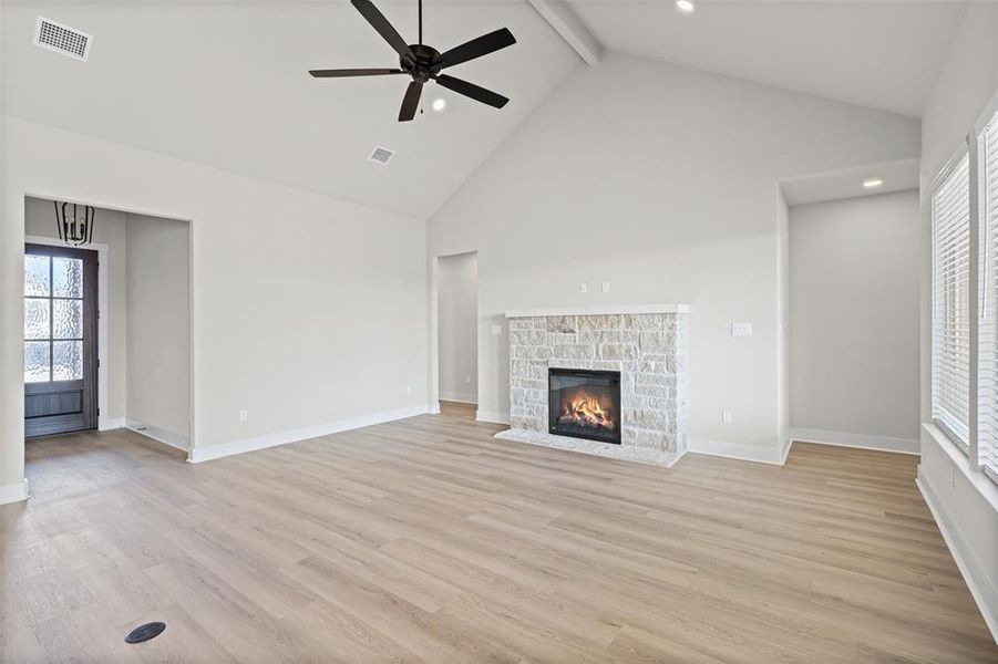 Unfurnished living room with plenty of natural light, high vaulted ceiling, a ceiling fan, beamed ceiling, and light wood-type flooring