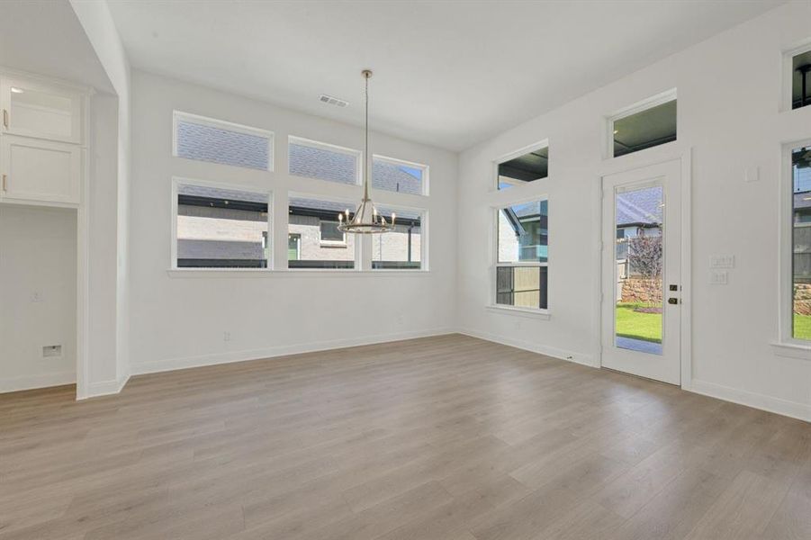 Spacious room featuring wood-finish flooring, white walls, and a contemporary chandelier