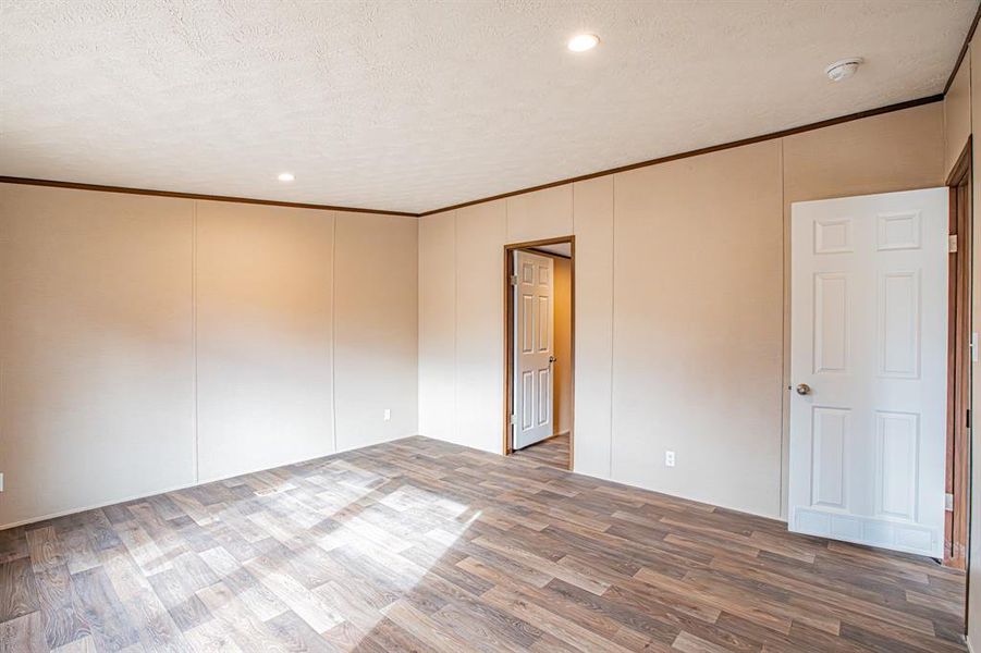 Empty room with wood-type flooring, a textured ceiling, and ornamental molding Empty room with wood-type flooring, a textured ceiling, and ornamental molding