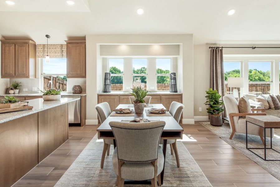 Open-concept dining area with wood-look floors connecting to kitchen and living room with large windows