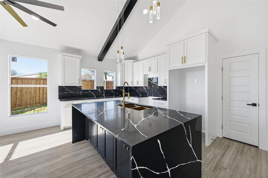 Kitchen featuring dark cabinetry, a kitchen island with sink, white cabinetry, backsplash, and high vaulted ceiling Kitchen featuring dark cabinetry, a kitchen island with sink, white cabinetry, backsplash, and high vaulted ceiling
