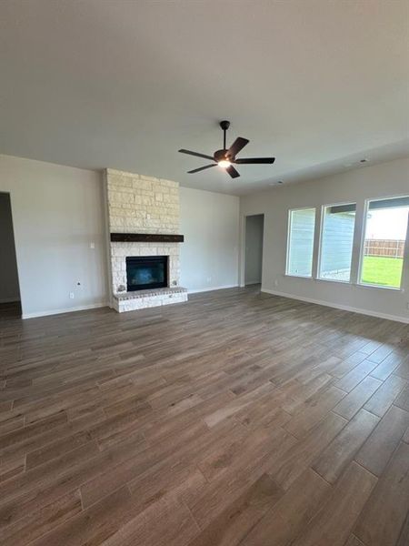 Spacious living area featuring wood-finish flooring, a stone fireplace with a dark wood mantel, and multiple windows