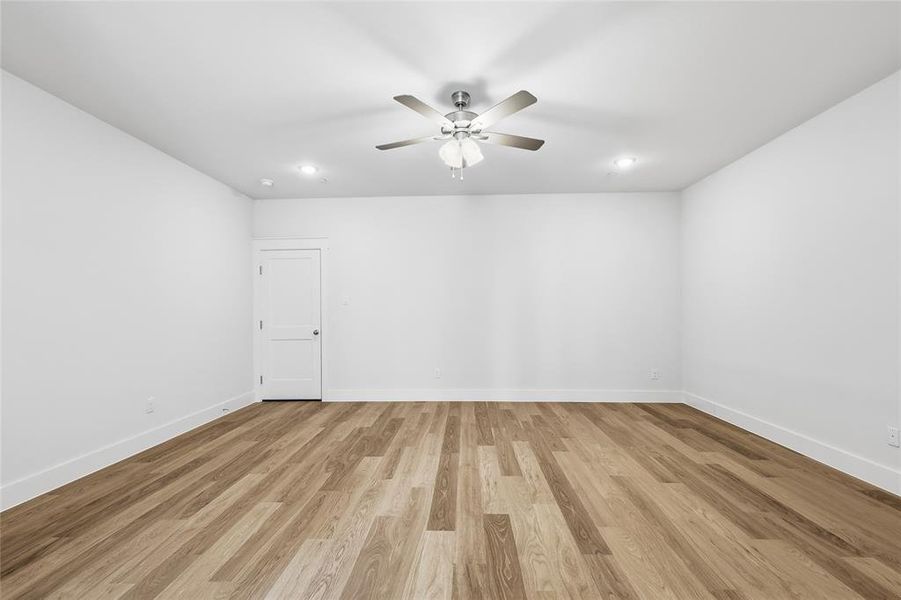 Spacious room featuring light wood flooring, white walls, and a ceiling fan with integrated lighting