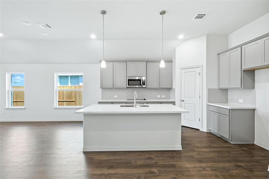 Kitchen with gray cabinetry, decorative backsplash, decorative light fixtures, light stone countertops, and dark wood-style flooring Kitchen with gray cabinetry, decorative backsplash, decorative light fixtures, light stone countertops, and dark wood-style flooring