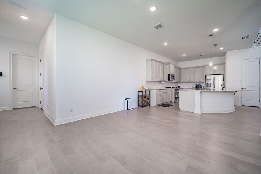 A contemporary kitchen and living area feature light wood flooring and a curved island for gathering.