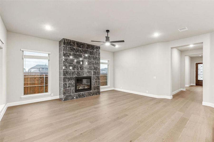 Open living room with dark stone fireplace, hardwood floors, and ceiling fan