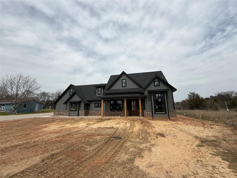 Modern farmhouse featuring brick siding, covered porch, driveway, and roof with shingles